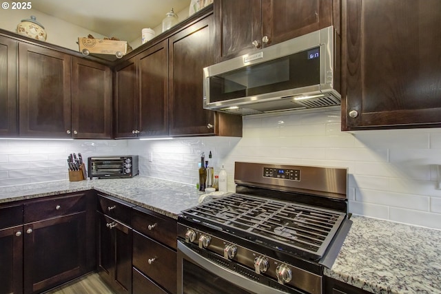 kitchen featuring dark brown cabinetry, a toaster, light stone counters, decorative backsplash, and stainless steel appliances