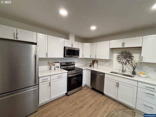 kitchen featuring appliances with stainless steel finishes, sink, white cabinets, and light wood-type flooring