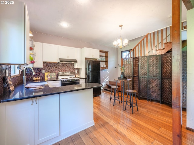 kitchen with decorative backsplash, gas range, dark countertops, freestanding refrigerator, and under cabinet range hood