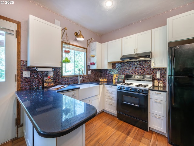 kitchen featuring range with gas cooktop, a sink, freestanding refrigerator, a peninsula, and under cabinet range hood