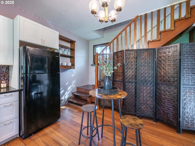kitchen featuring dark countertops, freestanding refrigerator, a notable chandelier, light wood-style floors, and white cabinetry