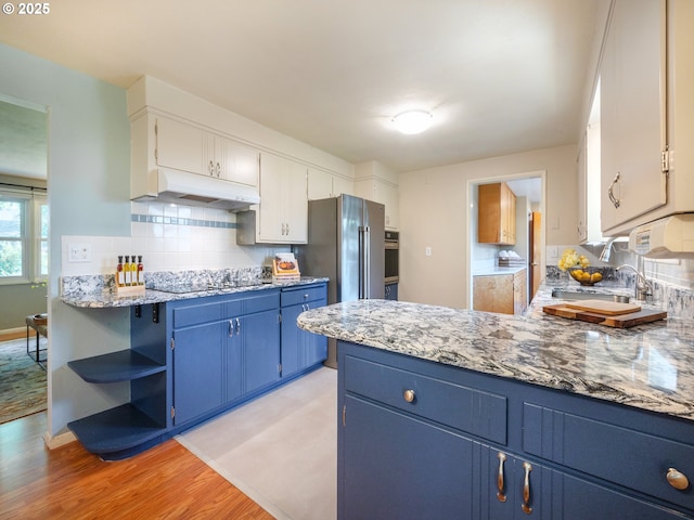 kitchen featuring a peninsula, under cabinet range hood, blue cabinets, light wood-style flooring, and backsplash