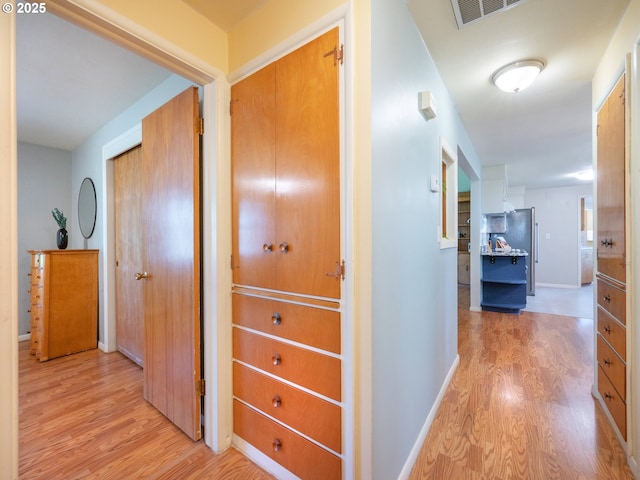 corridor with baseboards, visible vents, and light wood-type flooring