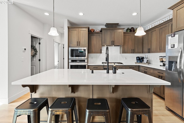 kitchen featuring light wood-style floors, appliances with stainless steel finishes, light countertops, and backsplash