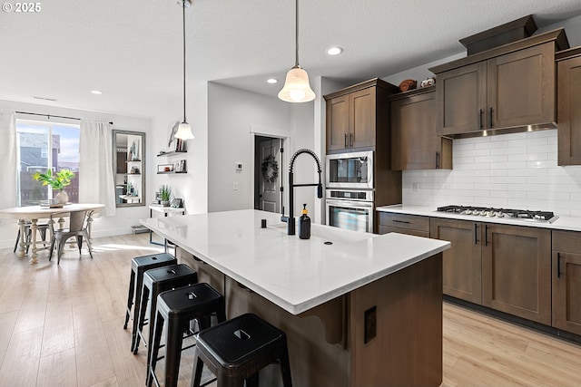 kitchen with a breakfast bar area, light wood finished floors, light countertops, backsplash, and appliances with stainless steel finishes