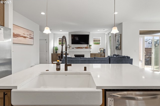 kitchen with appliances with stainless steel finishes, open floor plan, a fireplace, pendant lighting, and a sink