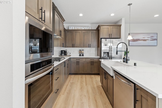 kitchen featuring pendant lighting, light wood finished floors, backsplash, appliances with stainless steel finishes, and a sink