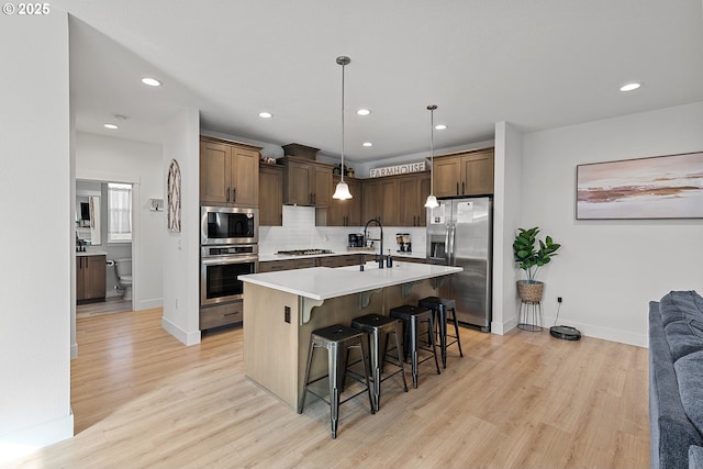 kitchen with appliances with stainless steel finishes, light wood-type flooring, light countertops, and tasteful backsplash