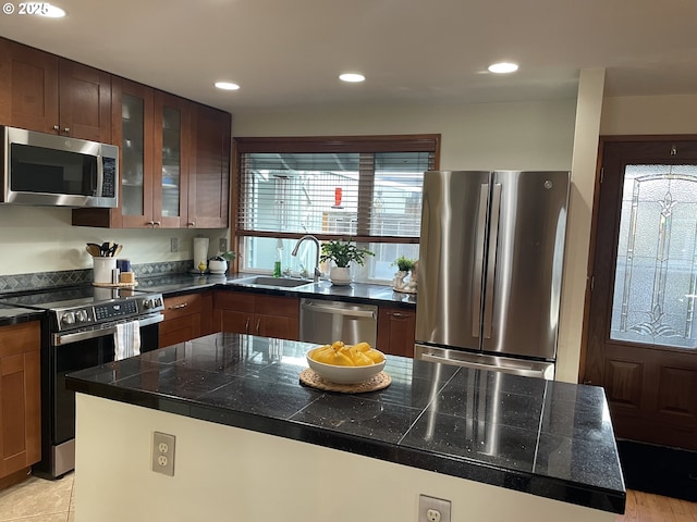 kitchen featuring a sink, recessed lighting, tile countertops, appliances with stainless steel finishes, and glass insert cabinets