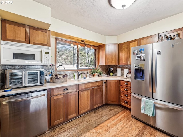 kitchen featuring sink, tasteful backsplash, a textured ceiling, light wood-type flooring, and stainless steel appliances