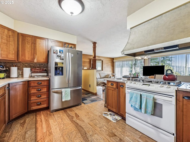 kitchen with tasteful backsplash, white range oven, light hardwood / wood-style floors, stainless steel refrigerator with ice dispenser, and wall chimney range hood