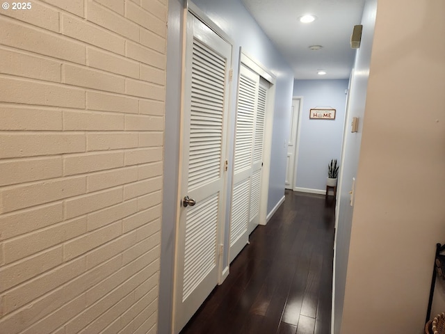 corridor with recessed lighting, baseboards, dark wood-style floors, and brick wall