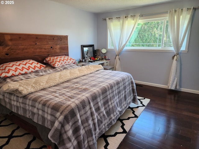 bedroom with visible vents, a textured ceiling, baseboards, and wood finished floors