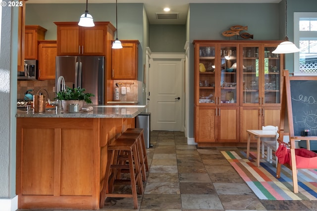 kitchen with stainless steel appliances, tasteful backsplash, brown cabinets, and dark stone counters