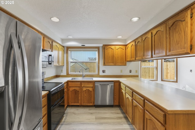 kitchen featuring sink, a textured ceiling, kitchen peninsula, stainless steel appliances, and light hardwood / wood-style floors