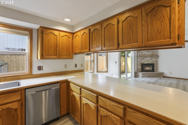 kitchen featuring a brick fireplace, stainless steel dishwasher, light hardwood / wood-style floors, and kitchen peninsula