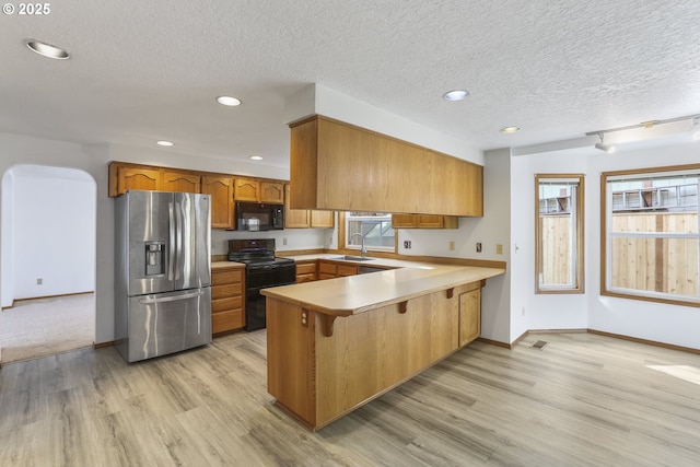 kitchen featuring sink, kitchen peninsula, light wood-type flooring, and black appliances