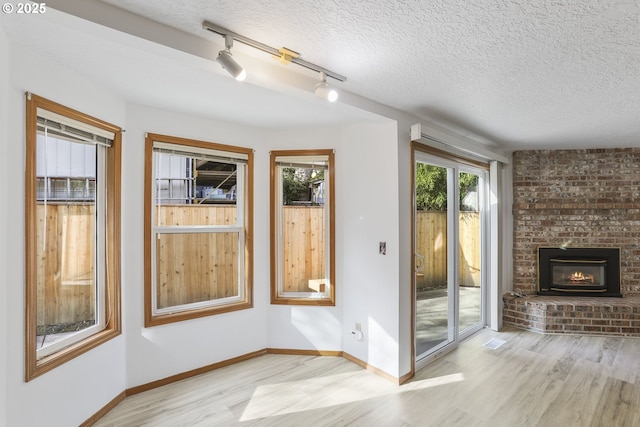 doorway to outside featuring a brick fireplace, light hardwood / wood-style floors, and a textured ceiling