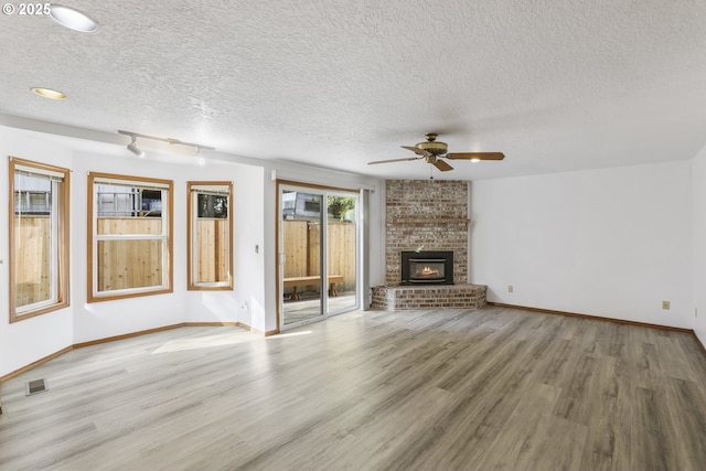 unfurnished living room featuring ceiling fan, wood-type flooring, track lighting, a textured ceiling, and a brick fireplace