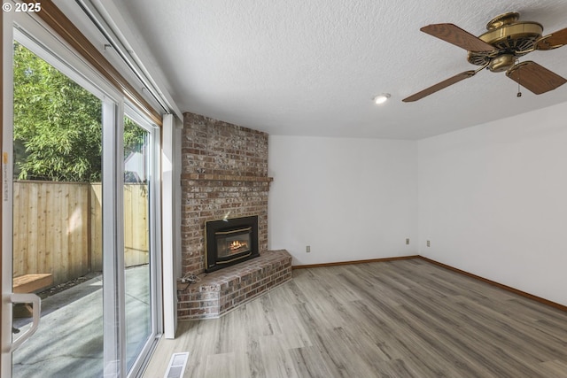 unfurnished living room featuring hardwood / wood-style floors, a textured ceiling, a brick fireplace, and ceiling fan