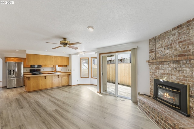 kitchen with sink, stove, kitchen peninsula, stainless steel refrigerator with ice dispenser, and light wood-type flooring