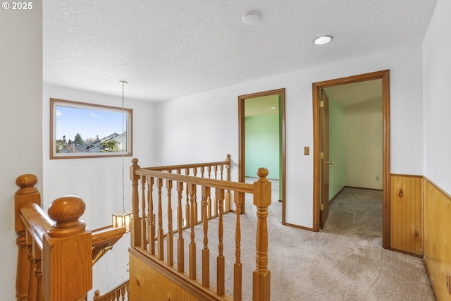 hallway featuring light carpet, a textured ceiling, and wood walls