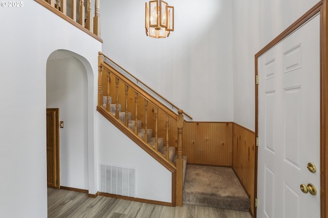 stairs with a high ceiling, wood-type flooring, and wooden walls