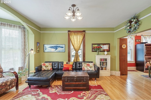 living room featuring a chandelier, light wood-type flooring, arched walkways, and baseboards