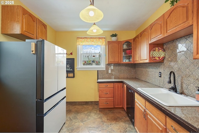 kitchen with glass insert cabinets, brown cabinets, decorative light fixtures, freestanding refrigerator, and a sink