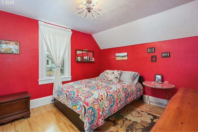 bedroom featuring baseboards, a textured wall, light wood-style flooring, vaulted ceiling, and a textured ceiling