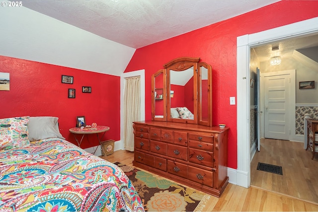 bedroom with light wood-type flooring, visible vents, vaulted ceiling, and a textured ceiling