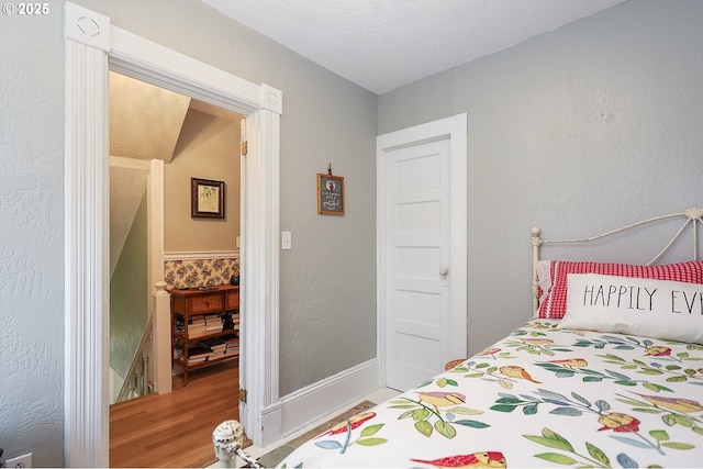 bedroom featuring baseboards, wood finished floors, and a textured wall