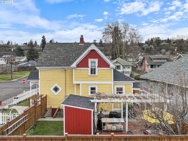 rear view of house with a fenced backyard, a residential view, a chimney, roof with shingles, and a pergola