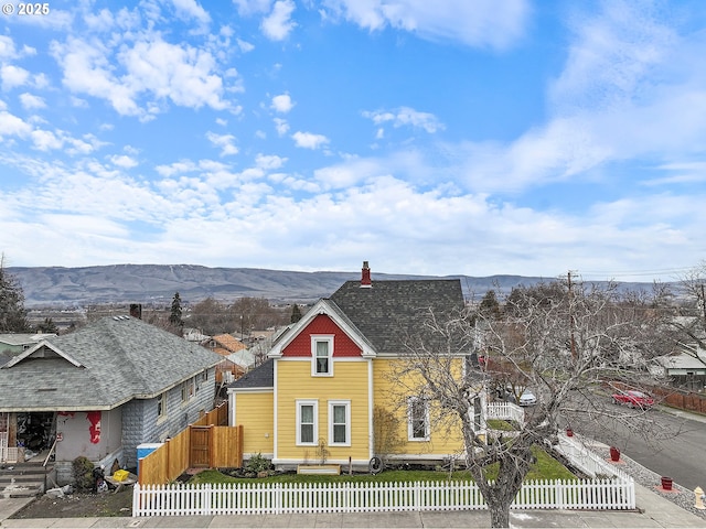 view of front facade featuring roof with shingles, a fenced front yard, and a mountain view