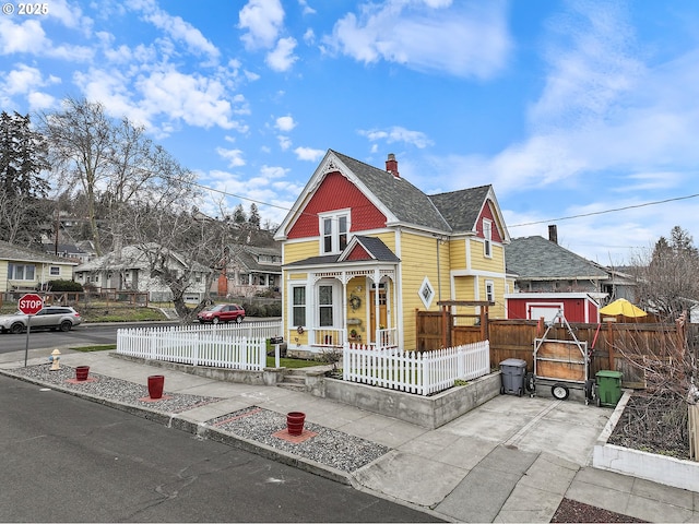 victorian-style house featuring a fenced front yard, a residential view, and a chimney