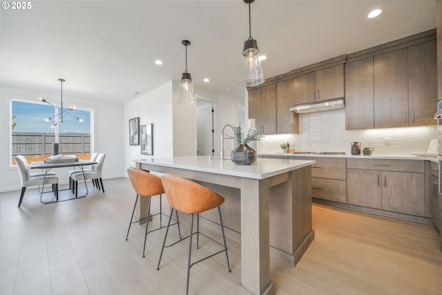 4308 N 12th Way, Ridgefield, WA 98642 - kitchen featuring light wood finished floors, stainless steel gas cooktop, light countertops, decorative backsplash, and under cabinet range hood