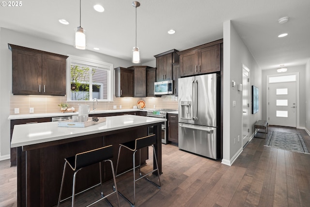 kitchen featuring dark brown cabinetry, backsplash, appliances with stainless steel finishes, wood finished floors, and light countertops