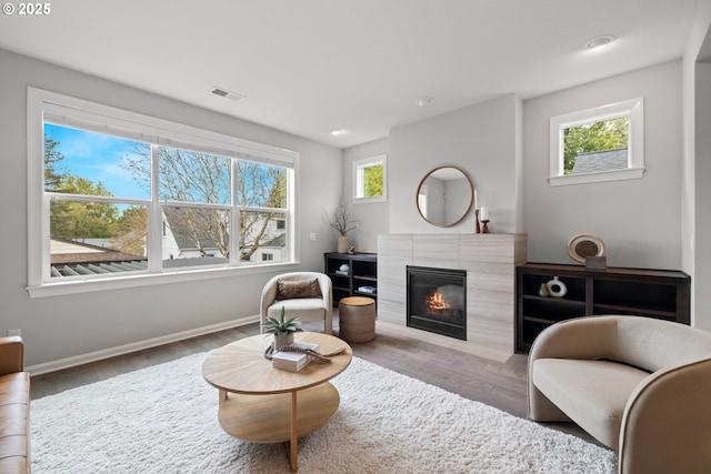 living room featuring visible vents, baseboards, wood finished floors, and a tile fireplace