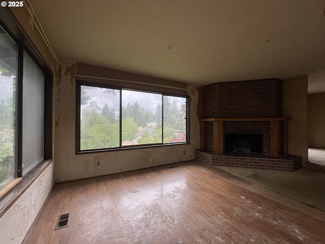 unfurnished living room featuring wood finished floors, healthy amount of natural light, and a brick fireplace