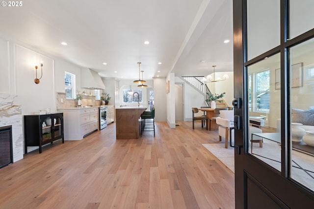 interior space featuring a kitchen breakfast bar, custom range hood, light countertops, light wood finished floors, and tasteful backsplash