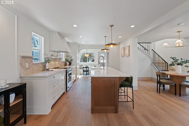 kitchen with light wood-style flooring, a breakfast bar area, high end range, custom exhaust hood, and backsplash