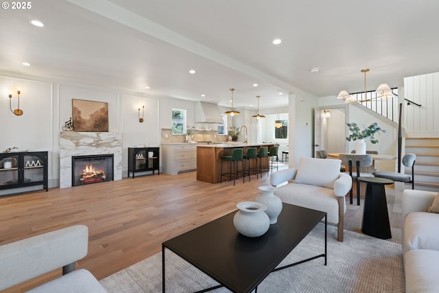 living area featuring light wood-style flooring, a notable chandelier, recessed lighting, a high end fireplace, and stairs