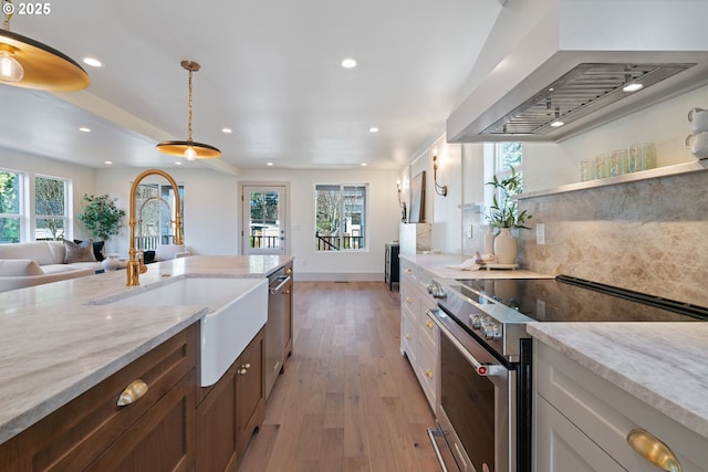 kitchen featuring light stone counters, stainless steel appliances, a sink, wall chimney range hood, and light wood-type flooring