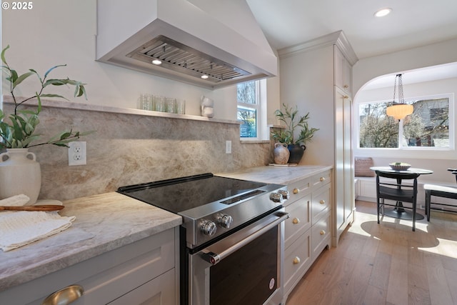 kitchen with light wood-style flooring, wall chimney range hood, stainless steel electric range, light stone countertops, and tasteful backsplash