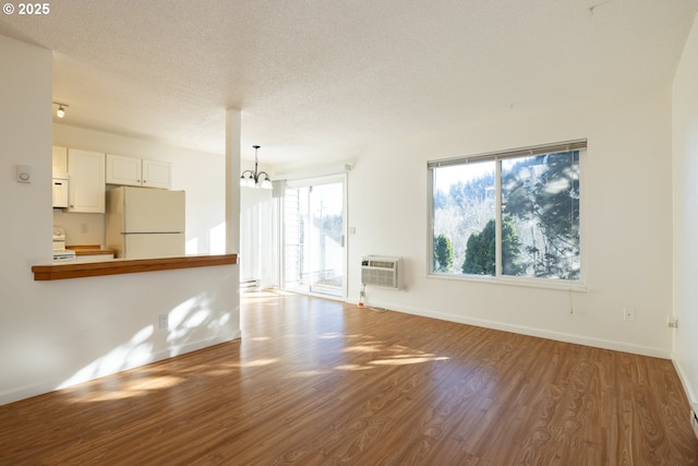 unfurnished living room featuring hardwood / wood-style flooring, a textured ceiling, a wall unit AC, and an inviting chandelier