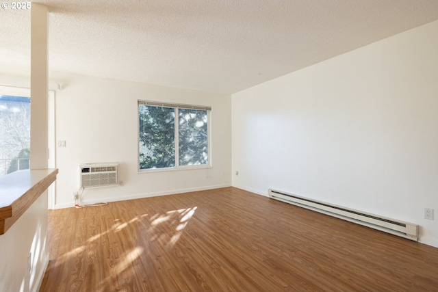 spare room with hardwood / wood-style floors, an AC wall unit, a textured ceiling, and a baseboard heating unit