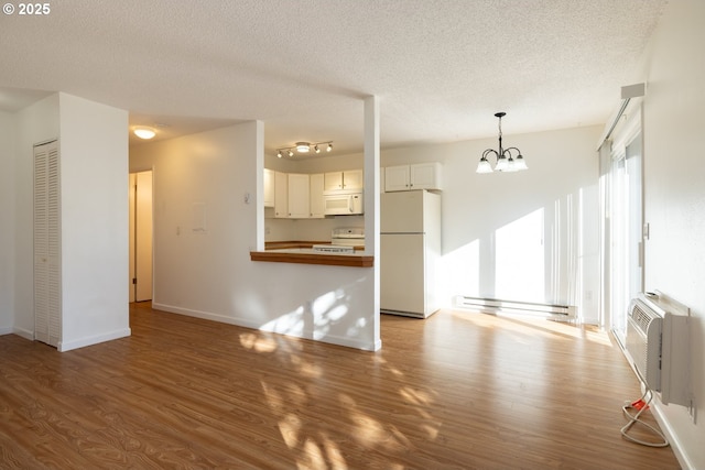 unfurnished living room with a textured ceiling, a wall unit AC, a baseboard heating unit, hardwood / wood-style flooring, and a notable chandelier