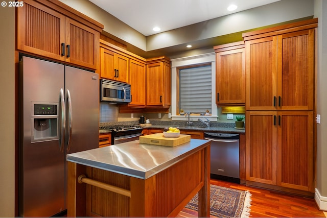 kitchen featuring appliances with stainless steel finishes, stainless steel counters, dark wood finished floors, brown cabinets, and a center island