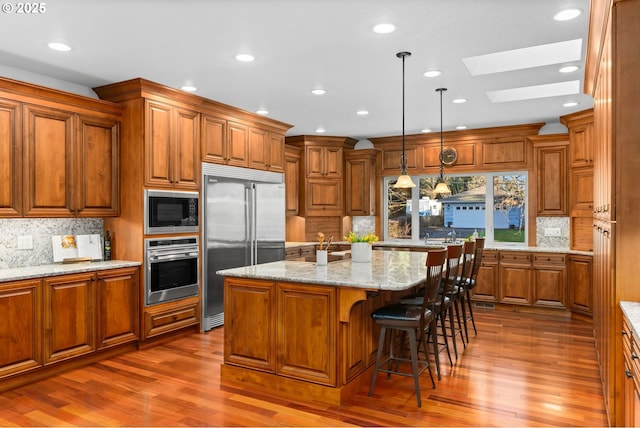 kitchen featuring dark hardwood / wood-style floors, pendant lighting, a center island with sink, built in appliances, and light stone counters