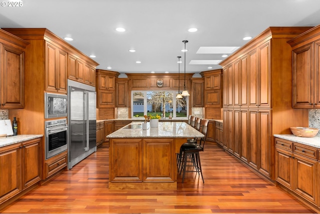 kitchen featuring a skylight, decorative light fixtures, built in appliances, a kitchen island, and light stone counters